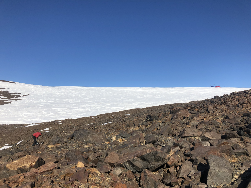 a scientists walks along a rocky path in antarctica, there is snow in the background